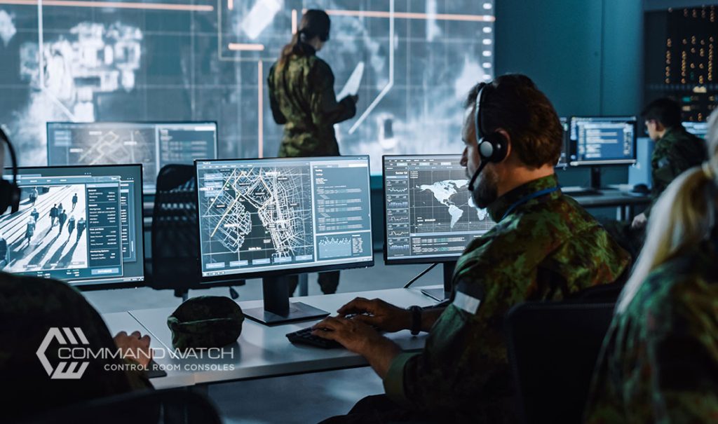 Military personnel in command center sitting in console desks and monitoring video walls and monitors